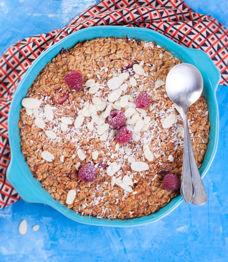 Raspberry coconut baked oats in a round dish topped with fresh raspberries, flaked almonds and toasted coconut